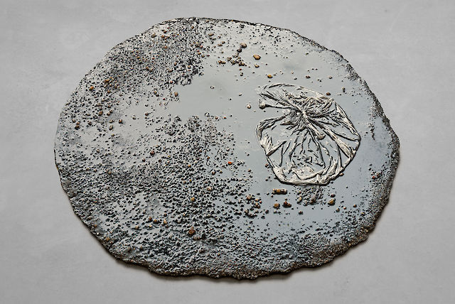 Marlie Mul, Puddle (Black Market), 2013, sand, stones, resin, plastic bag, 2 cm ø 80&nbsp;cm